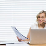 Beautiful woman talking on mobile phone while holding document at home